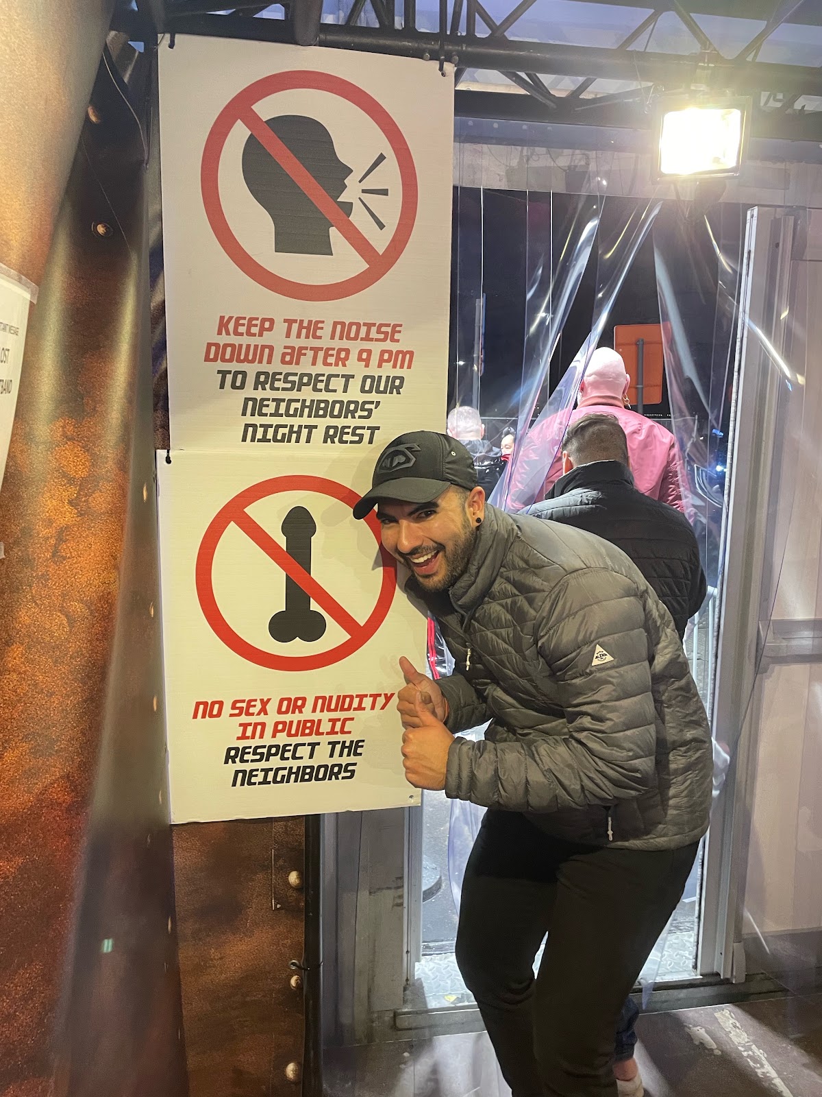 gay justfor.fans content creator phil standing at the exit of darklands 2024 beside signs that read keep the noise down after 9 pm to respect our neighbors night rest and no sex or nudity in publix respect the neighbors