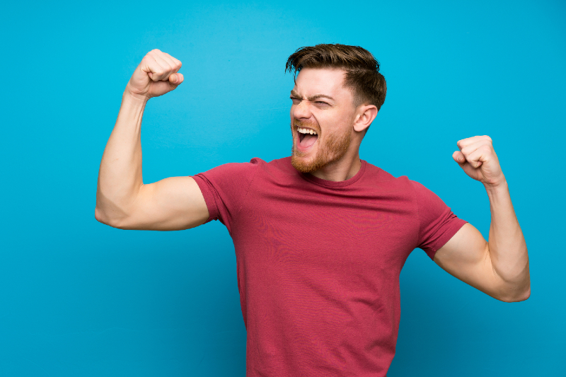 gay male in red shirt with his fists in the air getting excited about gay fisting technique and gay sex pleasure via AdobeStock