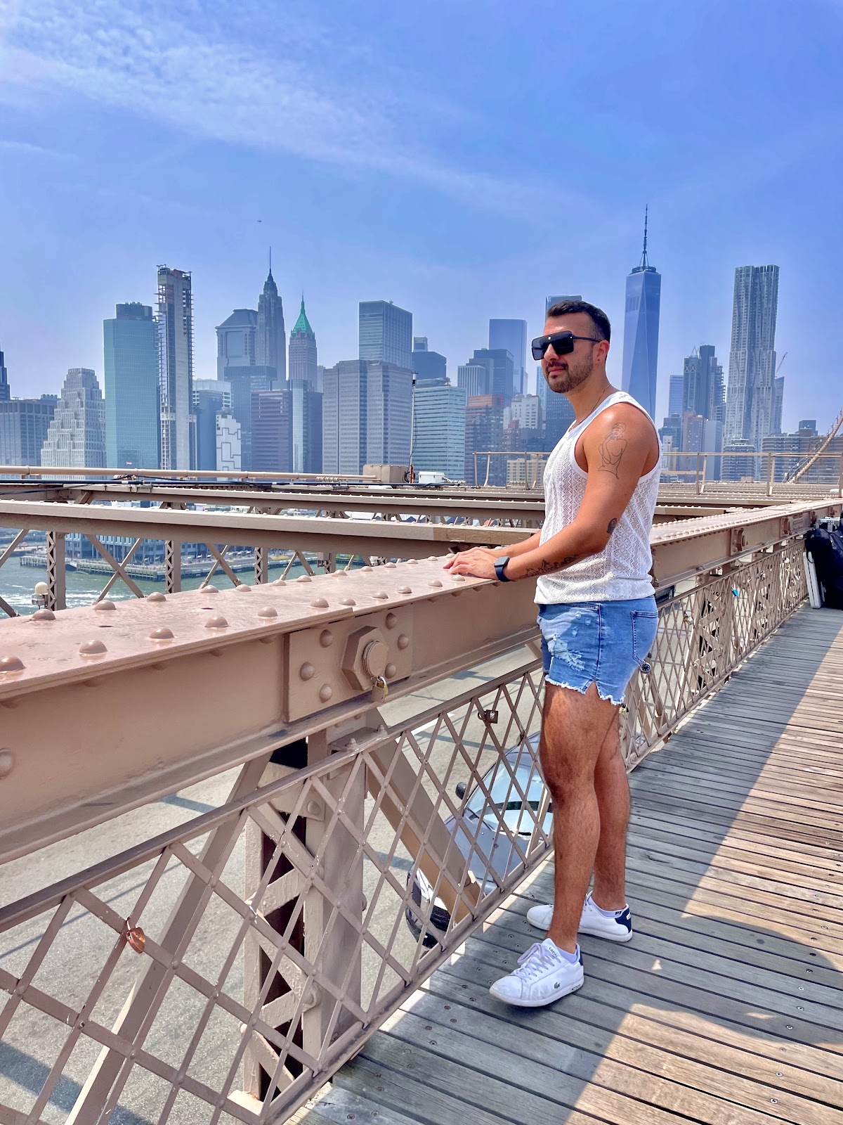 Gay male wearing tight white tank top and jean cut off shorts while standing on the brooklyn bridge of new york city