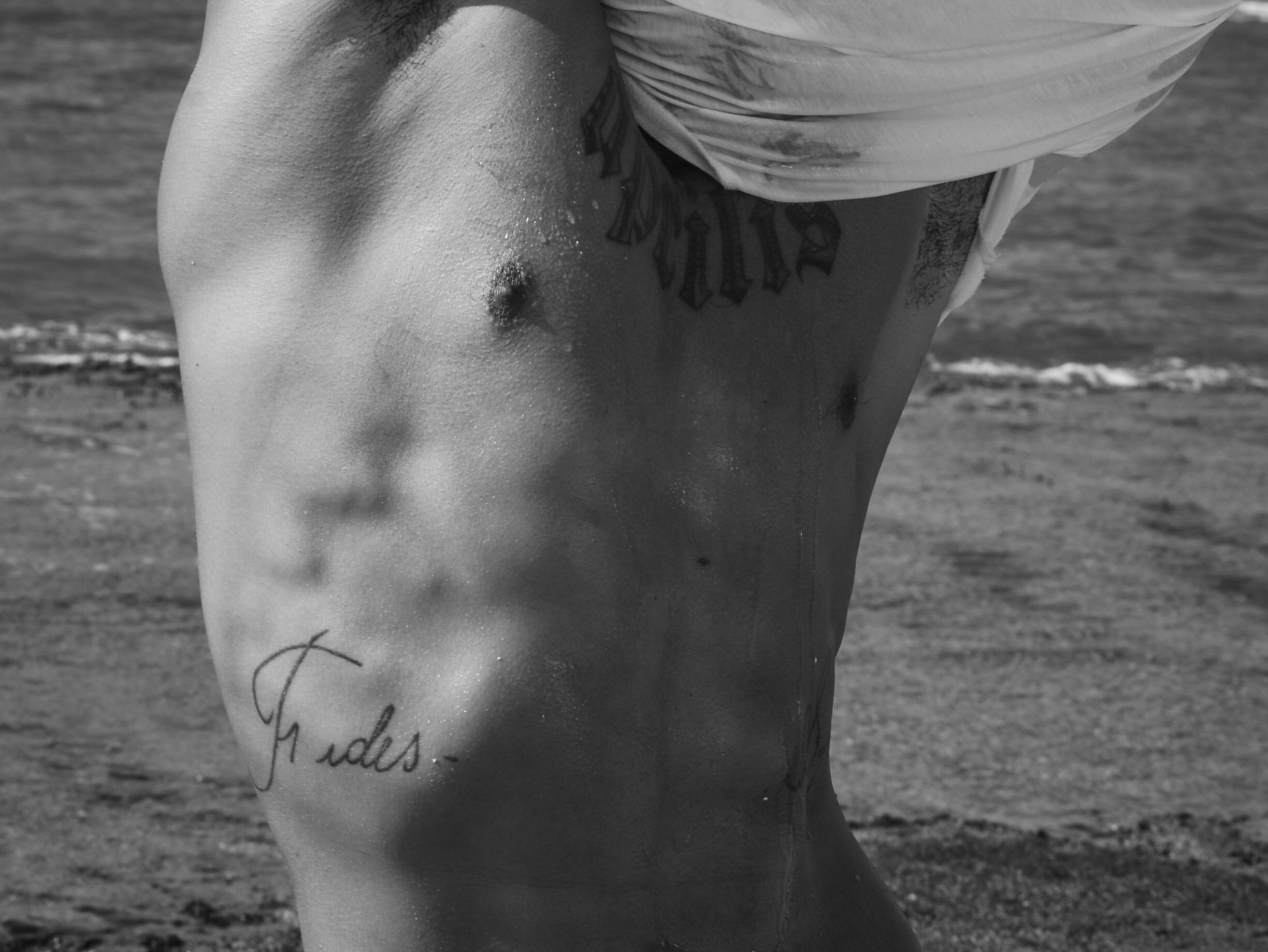 hot gay male taking off his white t-shirt at the beach ready for gay hookups in hot beach gay cruising Photo by Ricardo Diaz via Pexels