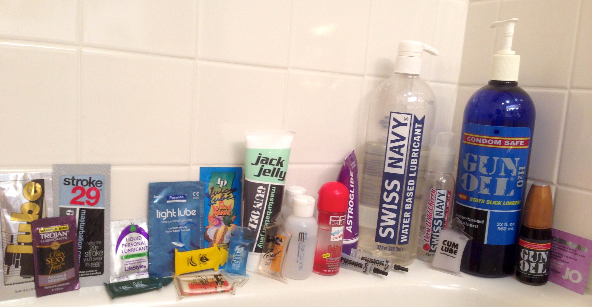 picture of gay lube brands lined up against the bathroom tub tiles; lubricant include Swiss Navy Gun Oil Jack Jelly ID lube JO and condoms -- image rights reserved by ed and eddie via flickr